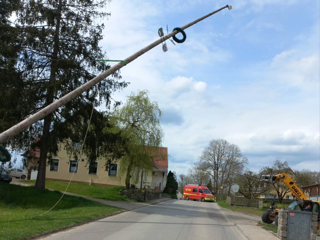 Aufgestellter Maibaum in einer Straßenlandschaft.