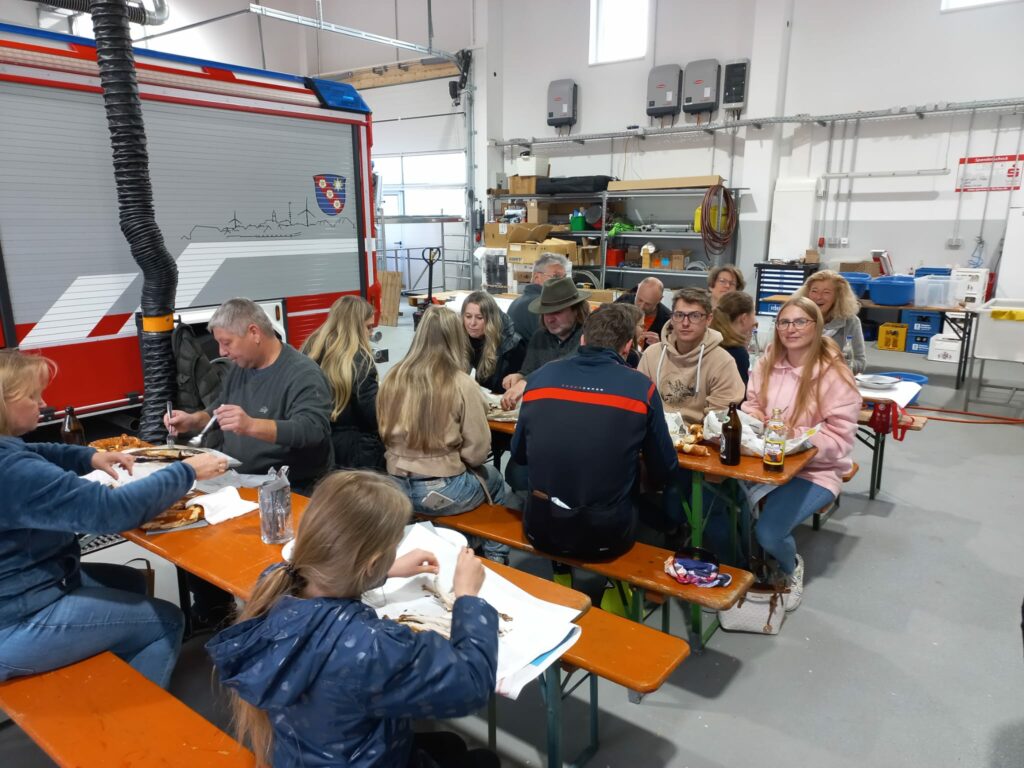 Gruppe isst in Feuerwehrstation an Tischen.