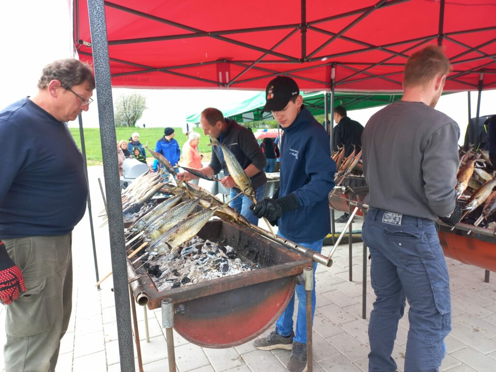 Männer grillen Fisch unter rotem Zelt.