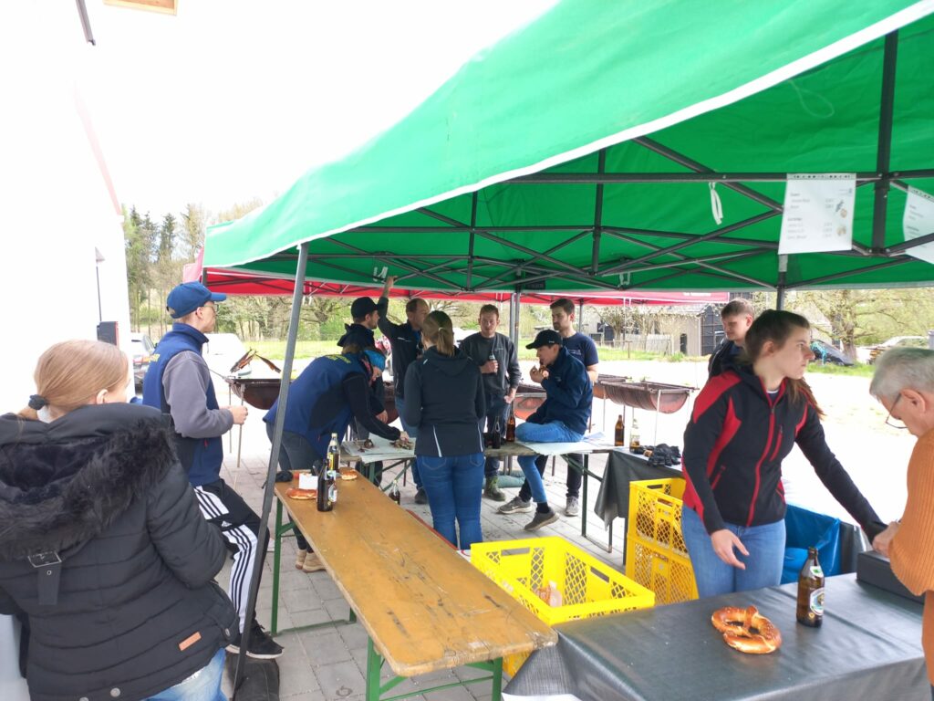 Personen grillen und essen unter Pavillon.