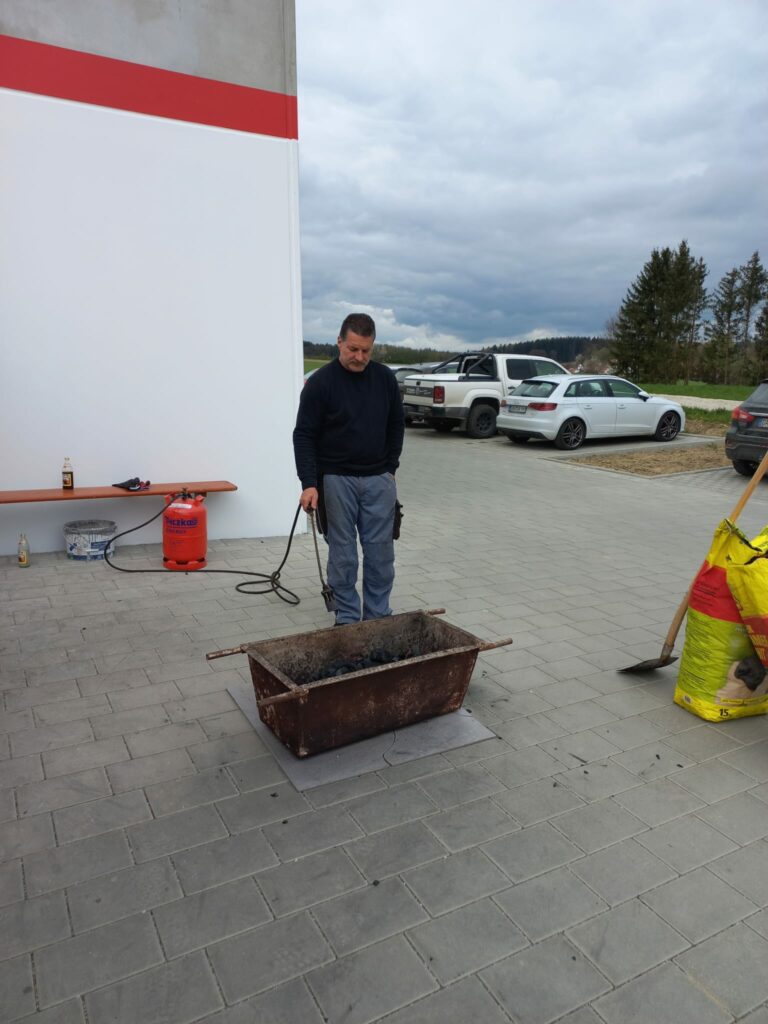 Mann steht neben Grill auf Betonboden.