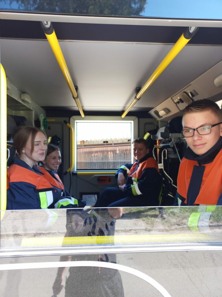 Jugendliche sitzen in einem Einsatzfahrzeug in Schutzkleidung.