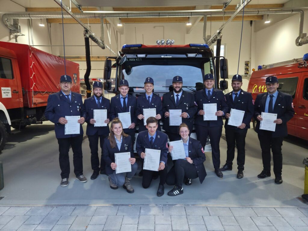 Feuerwehrleute mit Zertifikaten vor einem Feuerwehrwagen